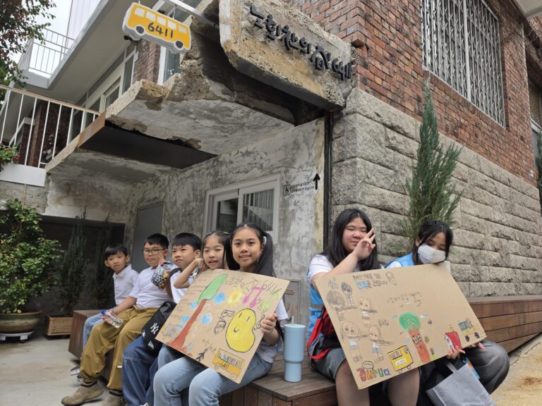 노회찬의 집 6411 앞에서 손그림 피켓을 들고 앉은 아이들